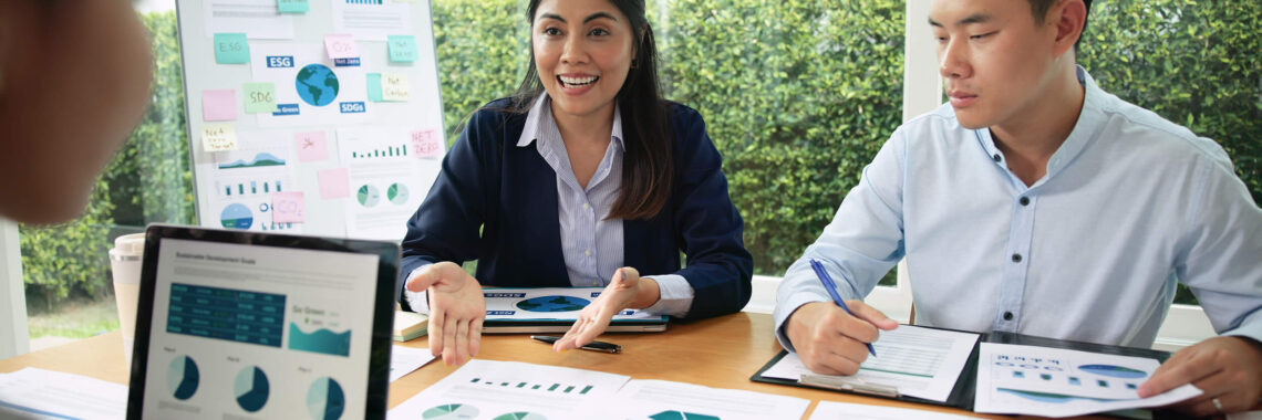 Reunião de profissionais analisando gráficos e dados de economia circular em papéis, quadro e tela de notebook.