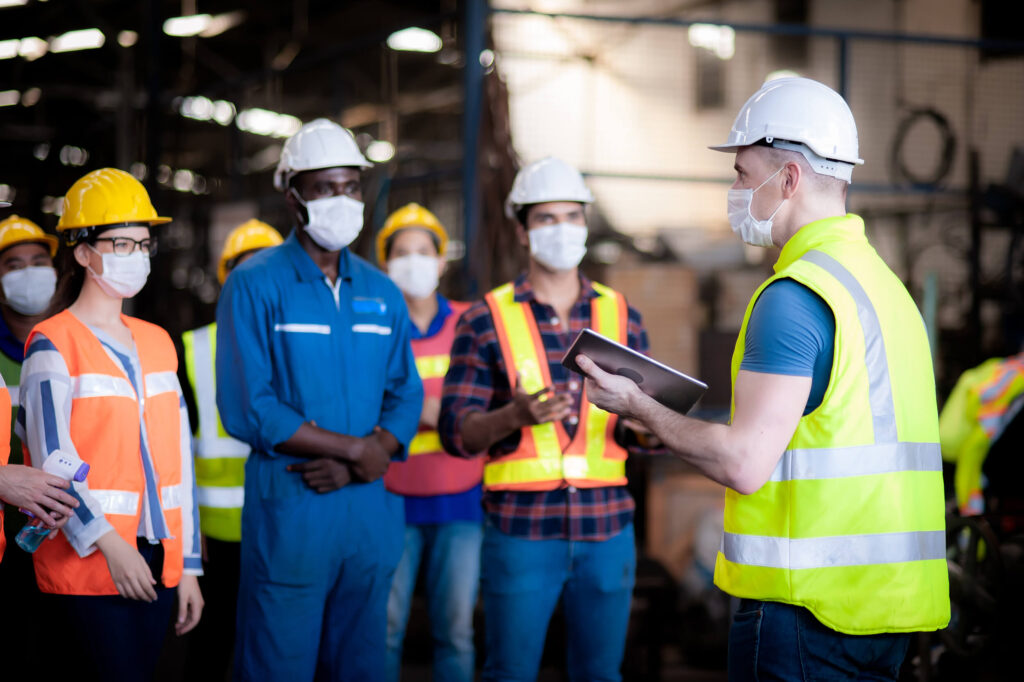 Profissionais usando capacete, colete e máscara em treinamento de segurança do trabalho.