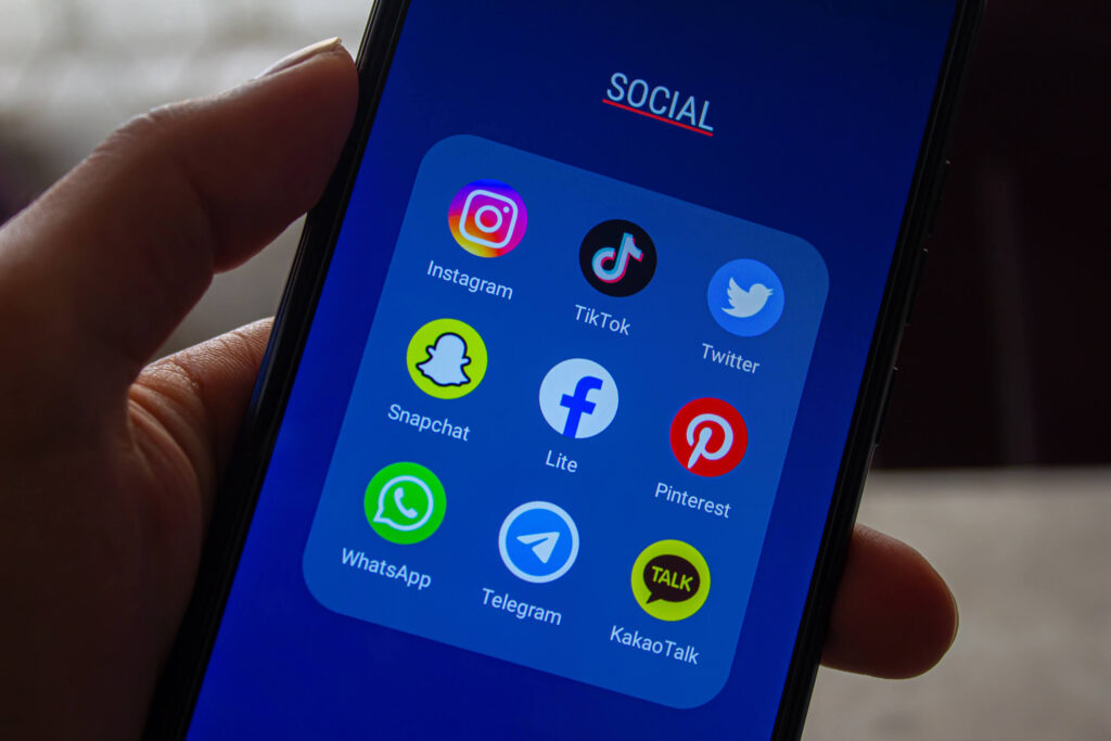 Pessoa segurando um telefone celular. Na tela, há ícones de redes sociais.