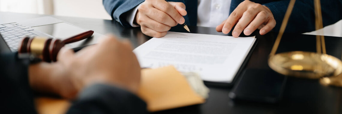 Advogado analisando e assinando contrato, com balança da justiça e martelo jurídico sobre a mesa.