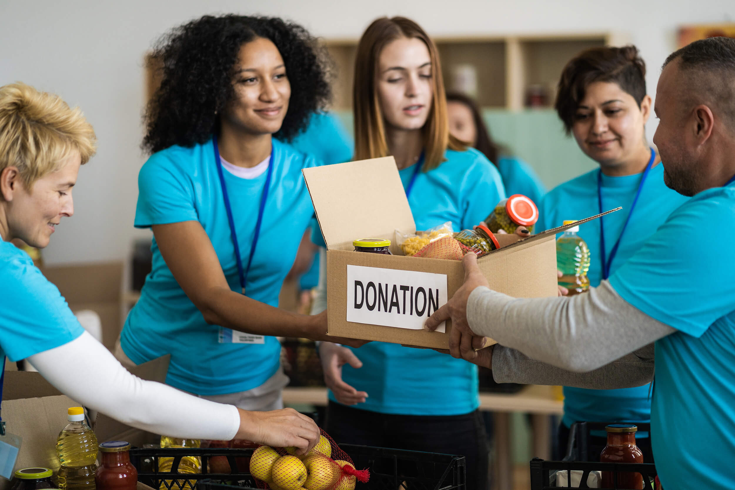 Voluntários de uma OSC segurando uma caixa de doação de alimentos.