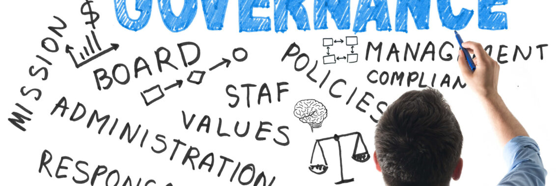 Homem de camisa azul de manga comprida escrevendo em um quadro branco com nuvem de palavras em inglês sobre governança: melhores práticas, comitês, missão, administração, responsabilidade, políticas, conformidade, gerenciamento.