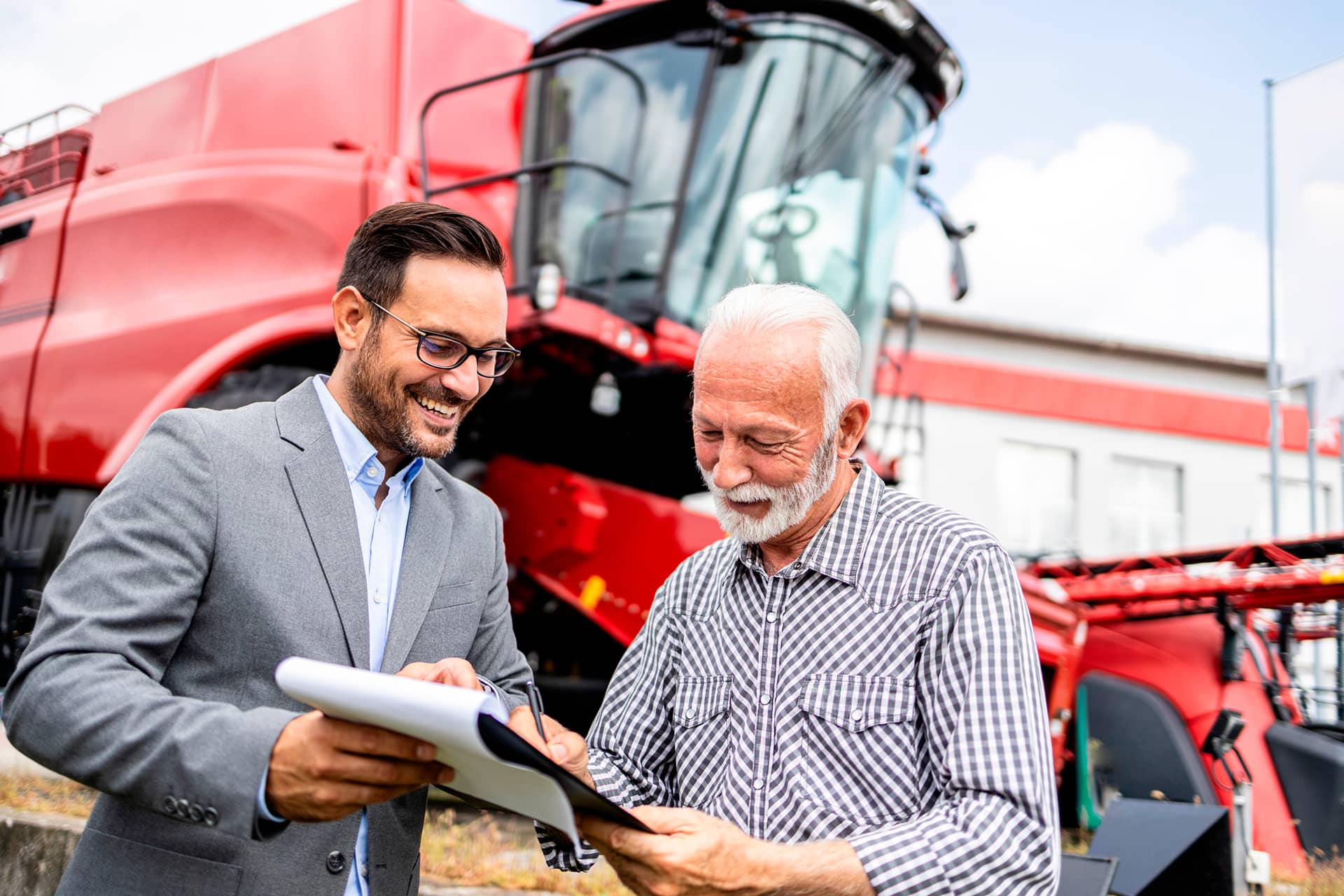 Consultor jurídico orientando produtor rural sobre documentos em frente a colheitadeira vermelha.